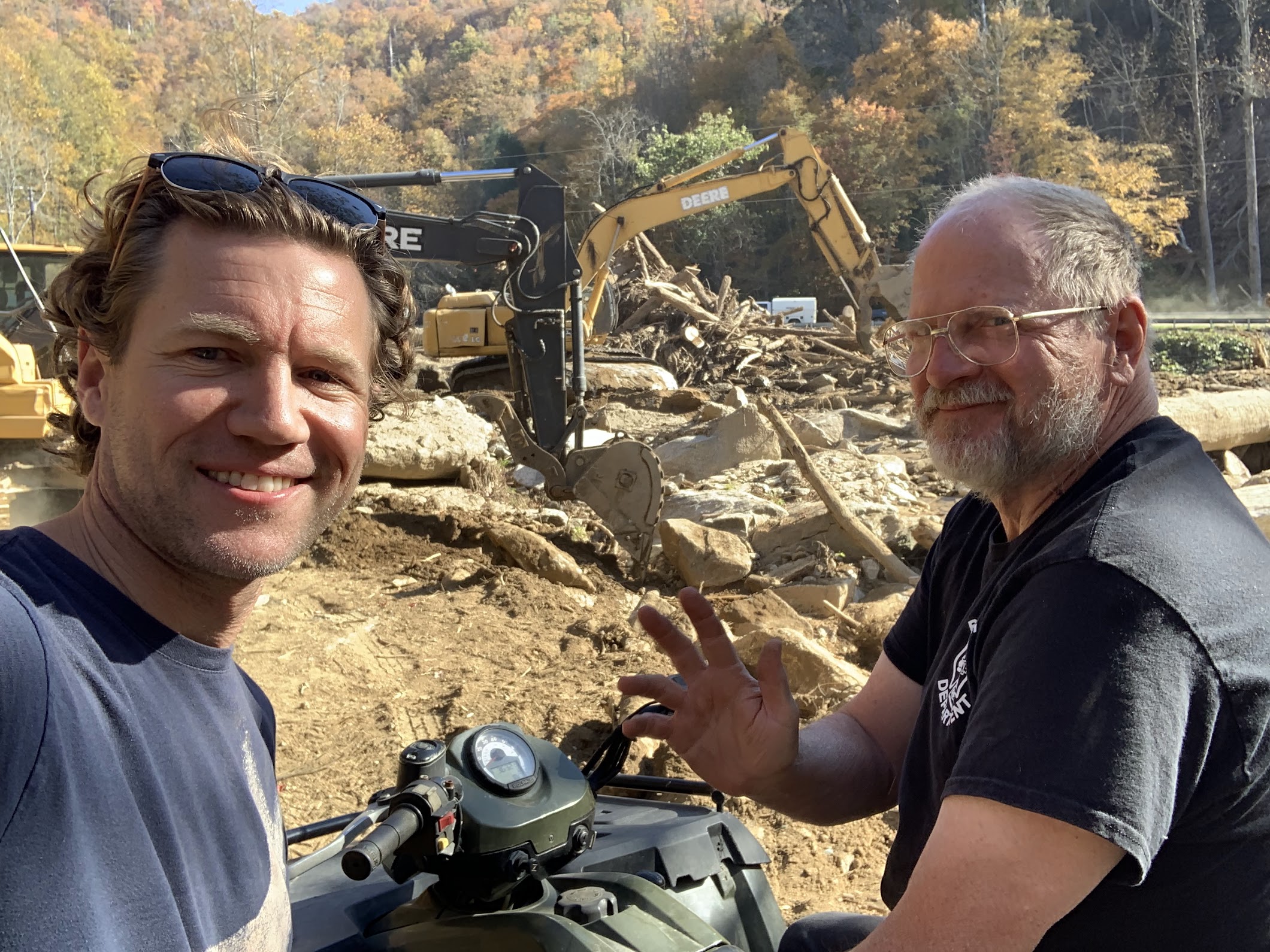 Two people in the foreground and in the background are diggers tearing up the ground.